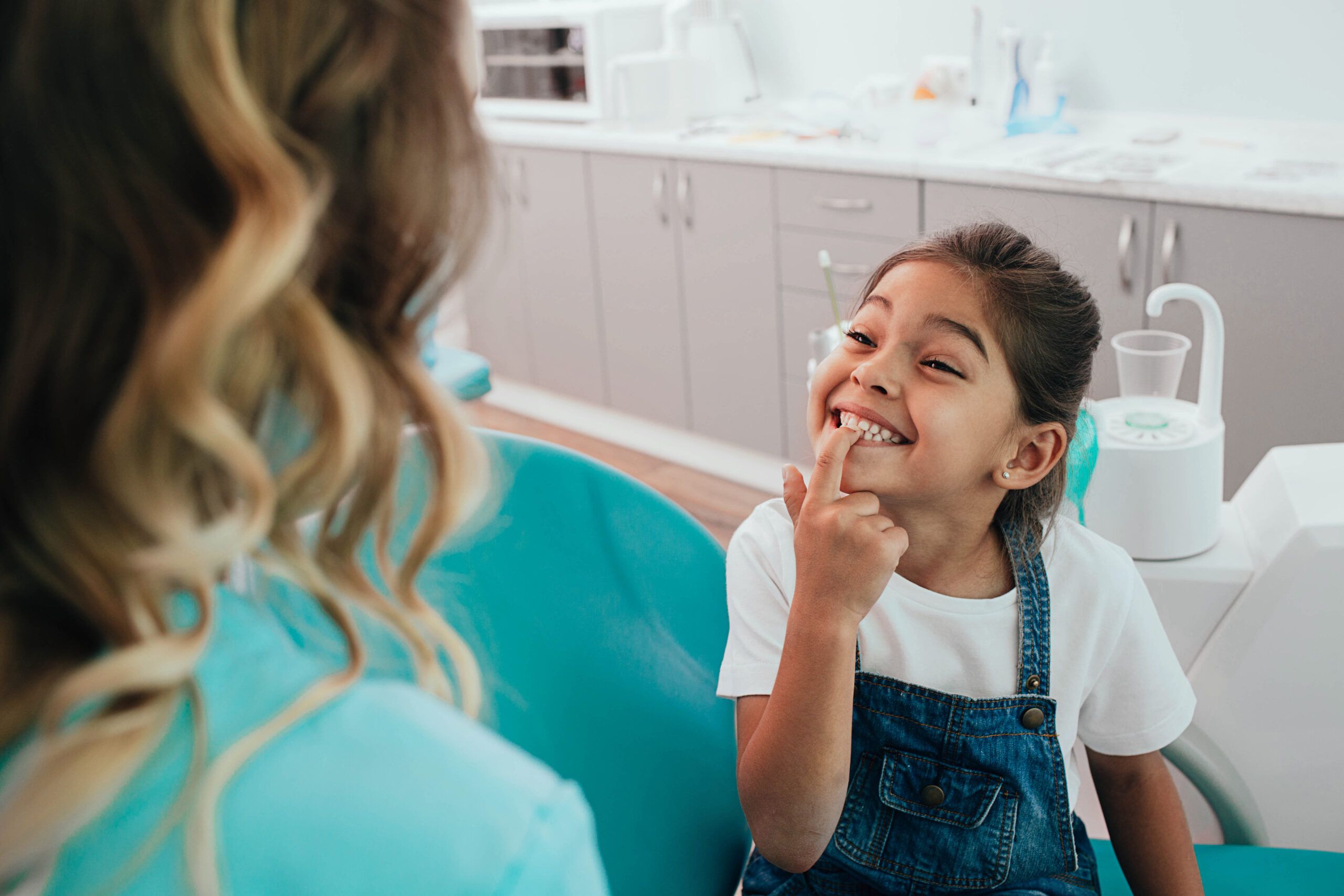 young girl smiling pointing to her teeth in the dental chair