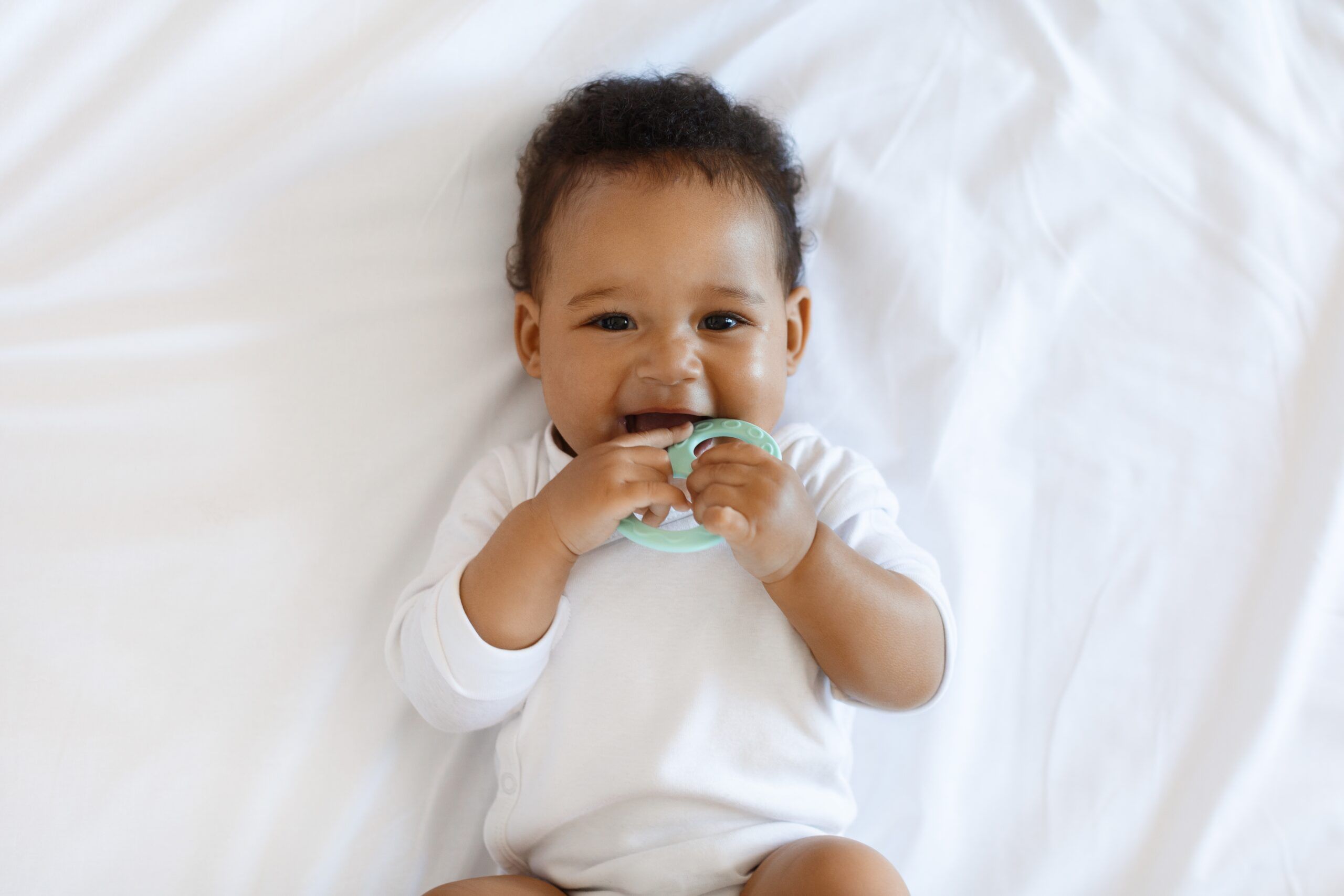 baby laying down teething on teething toy